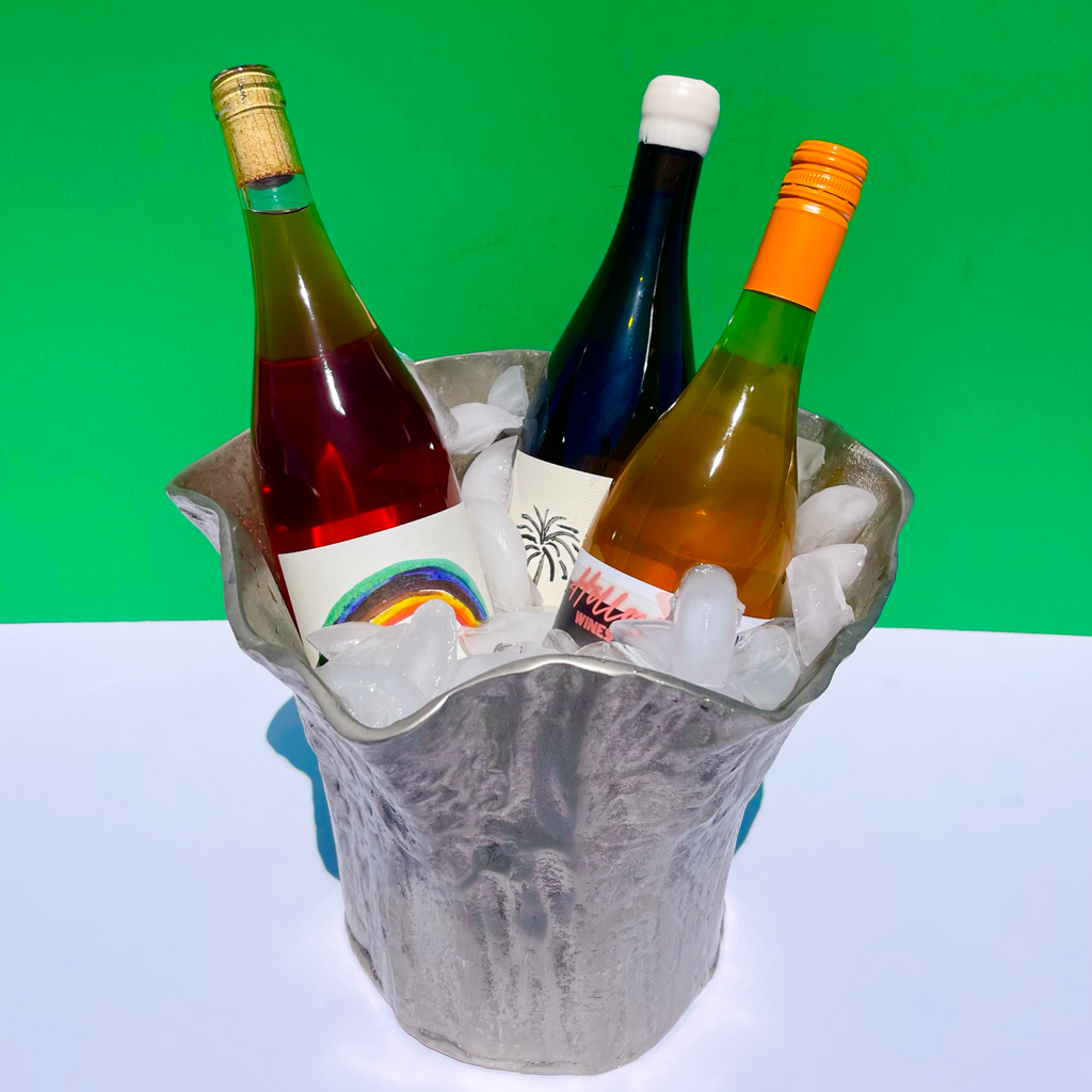 Three bottles of natural wine in a silver metal ice bucket with a green and white background.