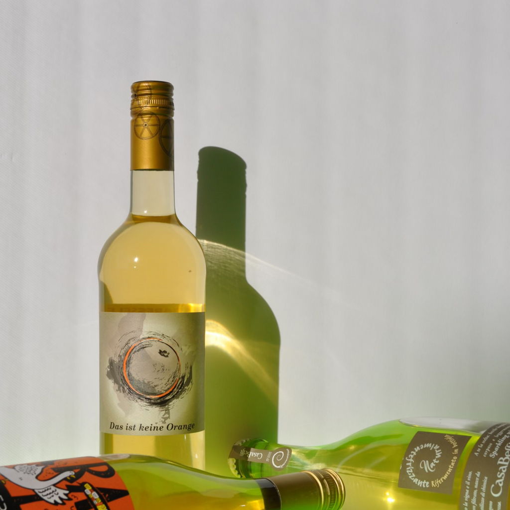 Photo of orange wine bottle with its reflection against a wall and other wine bottles laying around it.
