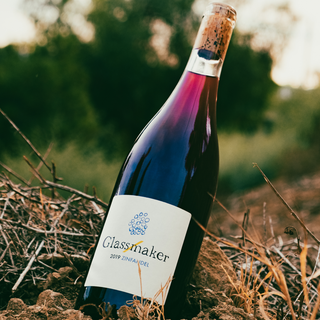 Phot of red wine bottles titled Glassmaker laying on grass with greenery in the background.