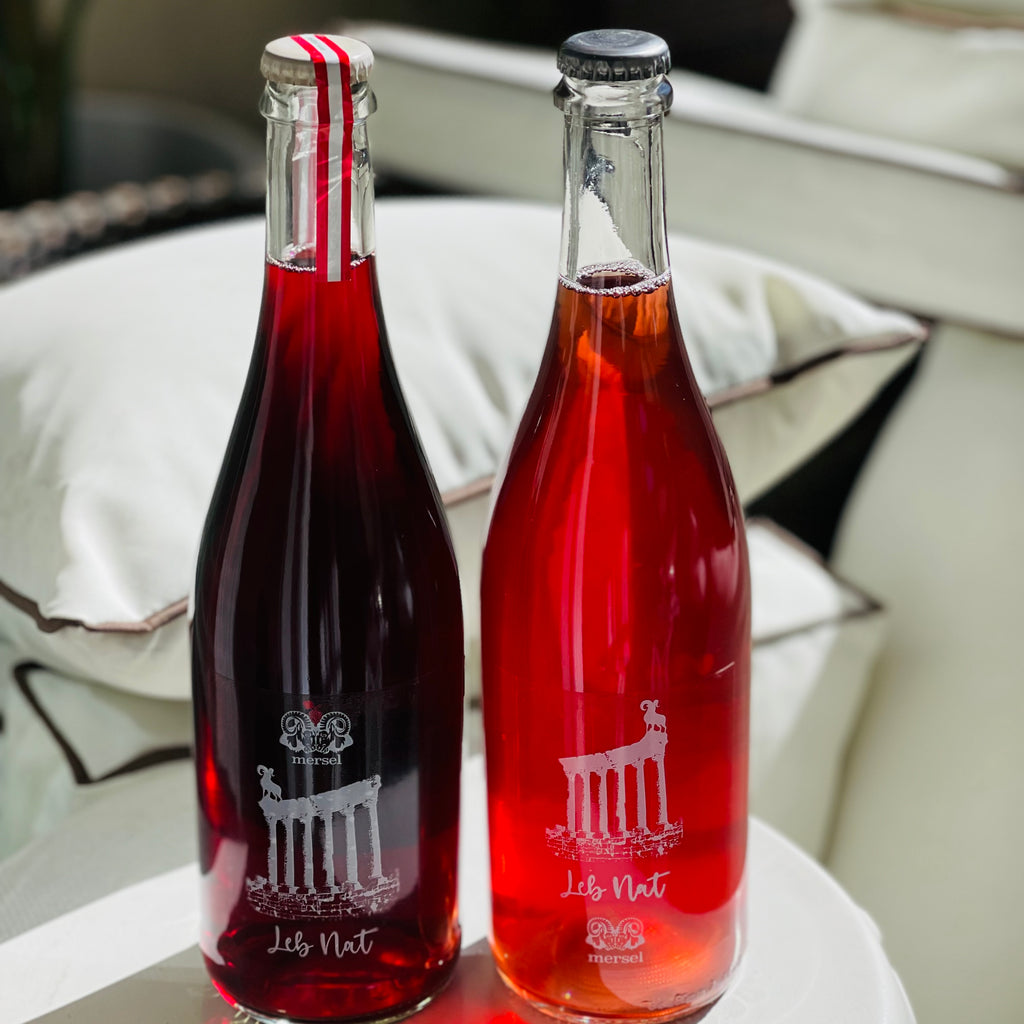A bottle of red and a bottle of rose wine on a white stool, with lounge chairs in the background.