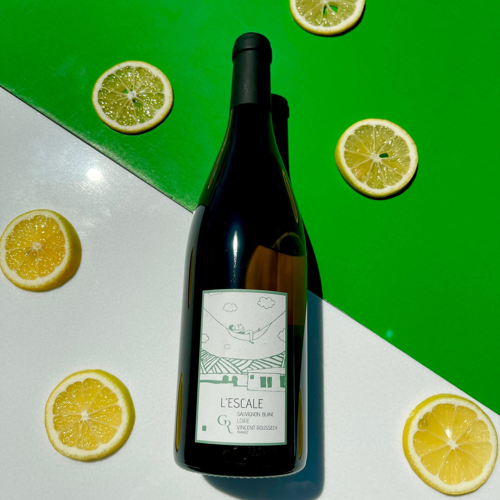 Bottle of sauvignon blanc surrounded by round lemon slices on green and white background.