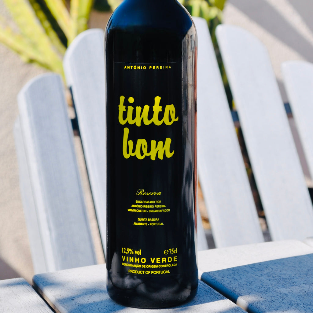 Photo of Tinto Bom Vinho Verde Red Wine shot on a wooden table with a wooden chair in the background.