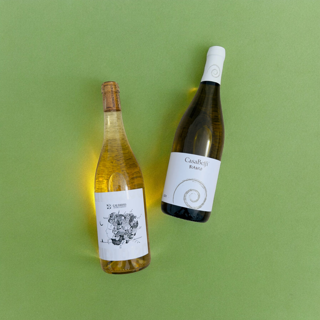 Two bottles of orange wine laying flat (for the blogpost) against a green background.