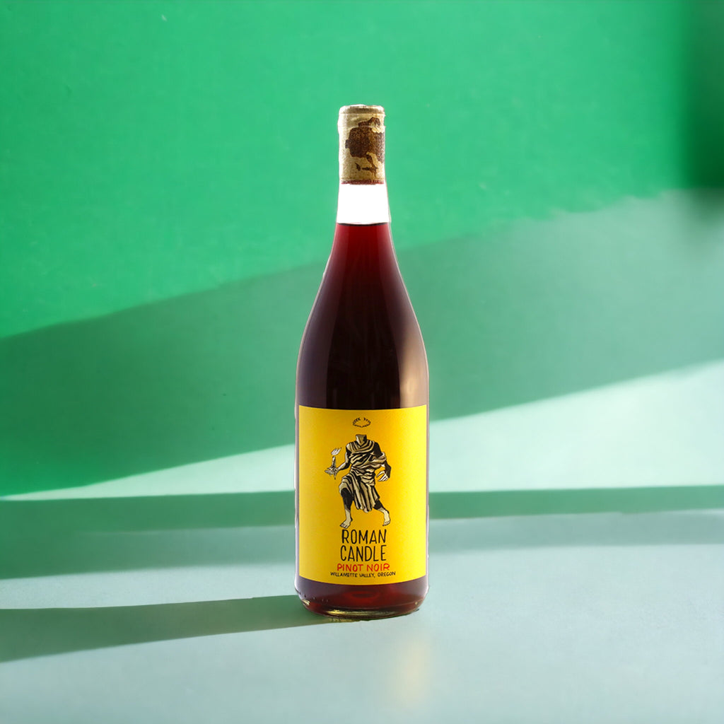 Roman Candle Pinot Noir bottle with a yellow label, shot against a green background.